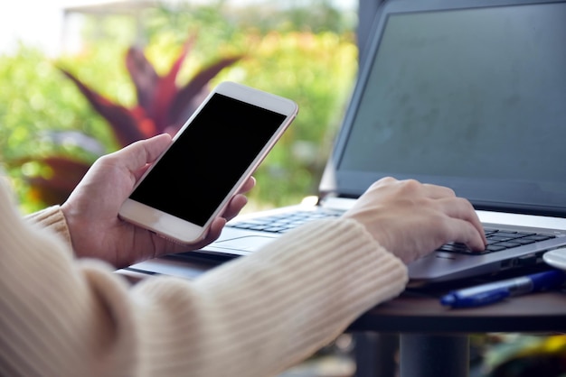 Foto gesneden handen van een vrouw met een laptop en een mobiele telefoon op tafel