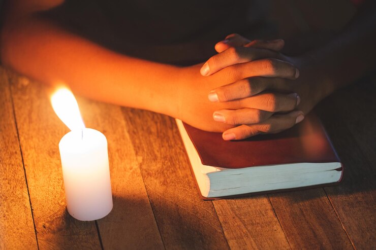 Foto gesneden handen van vrouw met kaars en bijbel op tafel