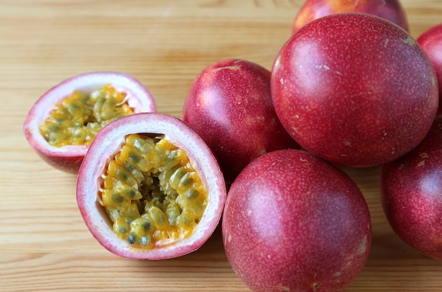 Gesneden in halve verse rijpe passievruchten met stapel hele vruchten op houten tafel