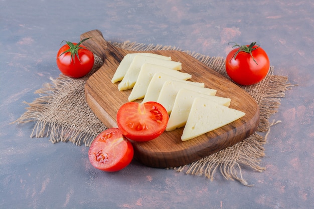 Gesneden kaas en tomaten op een snijplank op een jute servet, op de marmeren achtergrond.