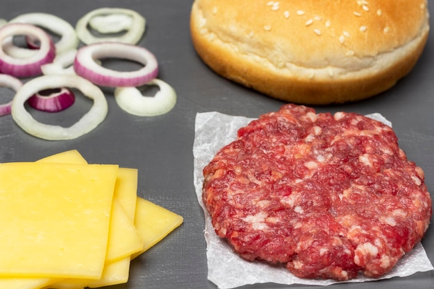 Gesneden kaas rauwe hamburger op papieren sesambroodje en gesnipperde ui op tafel