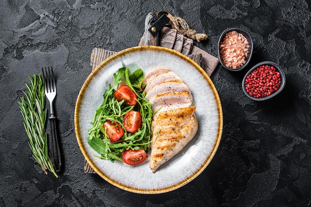 Gesneden kipfilet steak met groene salade in een bord. Zwarte achtergrond. Bovenaanzicht.