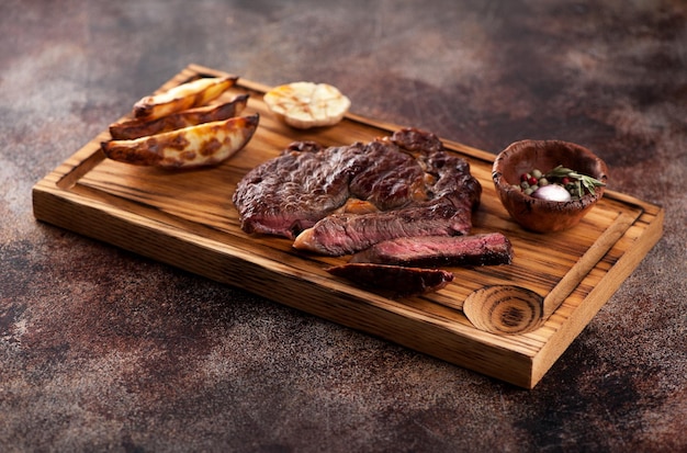 Gesneden medium zeldzame gegrilde biefstuk ribeye met gebakken aardappelen op een bruine roestige achtergrond