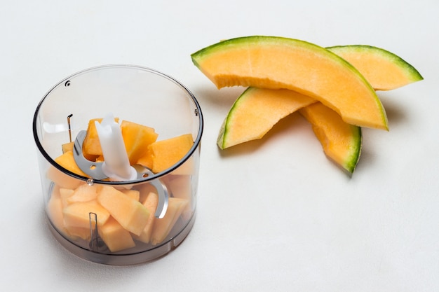 Gesneden meloen op tafel. Meloen in stukjes gesneden in blenderkan. Witte achtergrond. Plat leggen