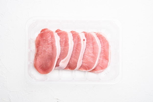 Gesneden rauw varkensvlees, in plastic verpakkingscontainer, op witte stenen tafelachtergrond, bovenaanzicht plat gelegd, met kopieerruimte voor tekst