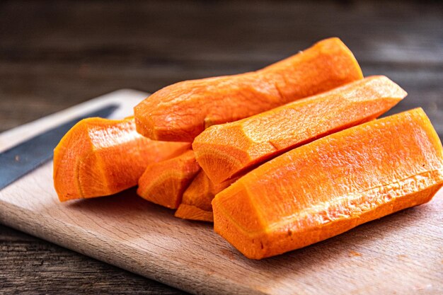 Gesneden rauwe zoete wortelen op een houten snijplank met een mes.