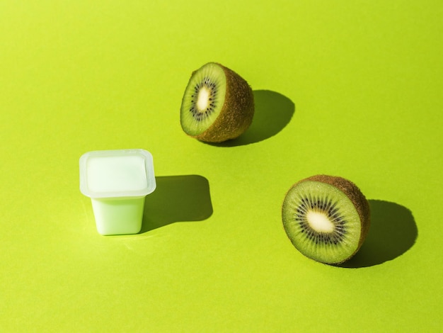 Gesneden rijpe kiwi en een kopje yoghurt op een groene achtergrond.