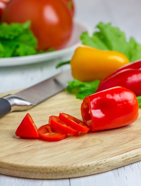 Gesneden rode paprika op de houten plank met kleurrijke groenten