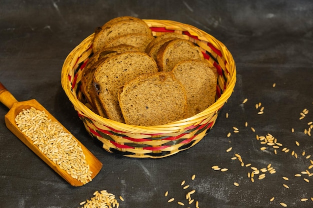 Gesneden roggebrood in een rieten mand Verspreid graan op een donkere achtergrond