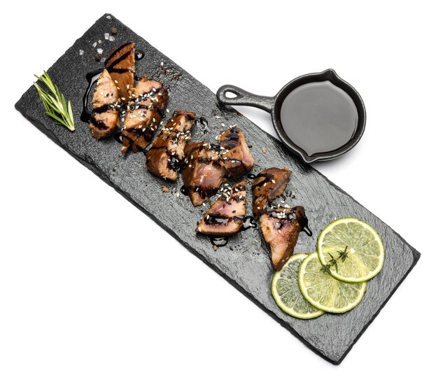 Gesneden stukjes biologische gegrilde tonijnsteak op een serveerbord van zwarte steen en teriyaki sojasaus