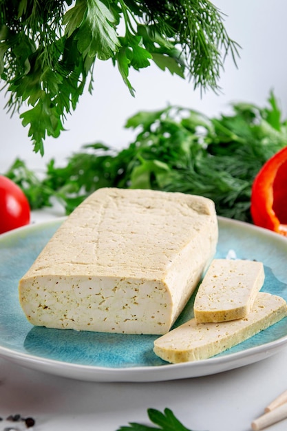 Gesneden tofu sojakaas op een snijplank met basilicum kruiden en groenten