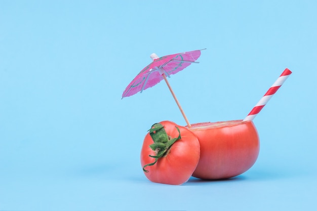 Gesneden tomaat met een cocktailparaplu en een rietje op een blauwe achtergrond.