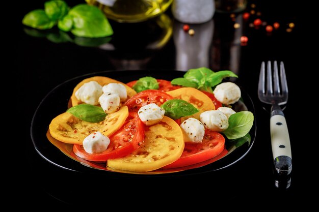 Gesneden tomaat met mozzarella, basilicum en kruiden op zwarte ondergrond.