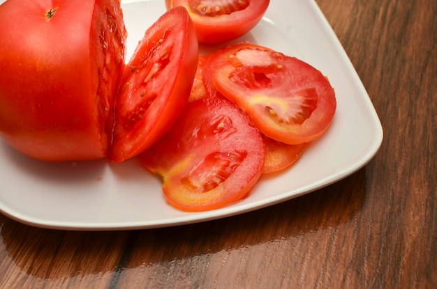 Gesneden tomaten in een witte plaat op een houten tafel met diagonaal bovenaanzicht