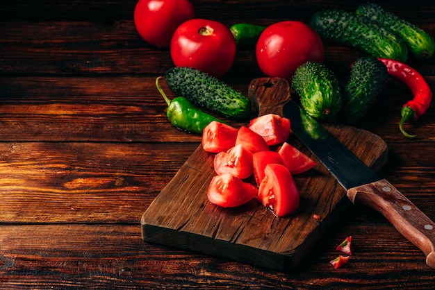 Gesneden tomaten op snijplank en komkommers met chilipeper