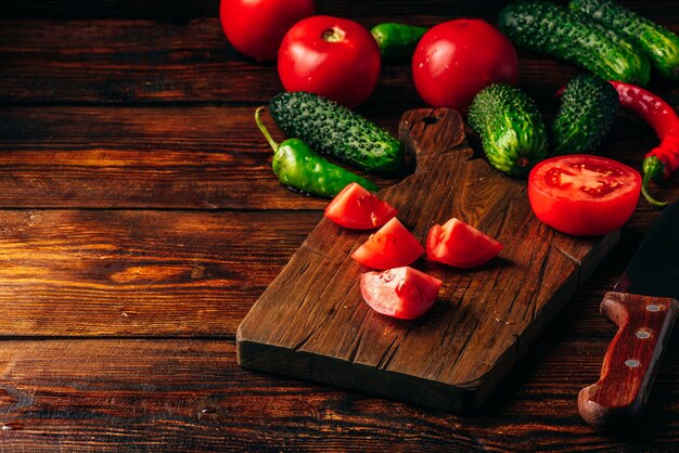 Gesneden tomaten op snijplank en komkommers met chilipepers over houten