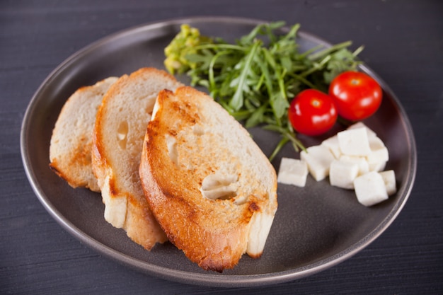 Gesneden Toostbrood op zwarte plaat met tomaten, feta en arugula