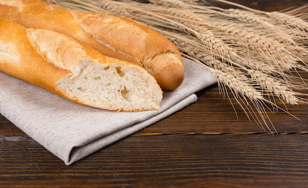 Gesneden vers Frans stokbrood doorgesneden om de textuur naast verse rijpe korenaren op een rustieke houten tafel te tonen, close-up