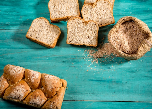 Gesneden volkoren brood en zakje met volkoren meel op getextureerd blauw hout, bovenaanzicht, ruimte voor tekst