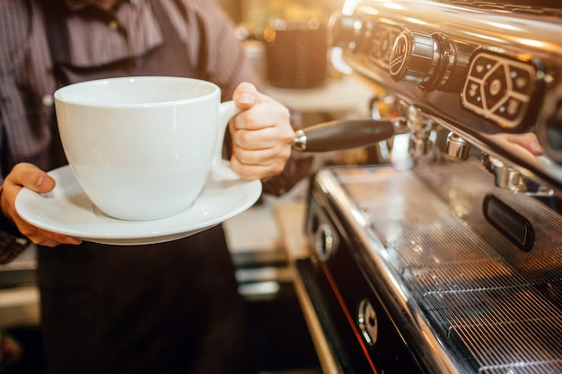 Gesneden weergave van barista met enorme witte kop koffie in handen. Hij staat in de keuken bij het koffiezetapparaat