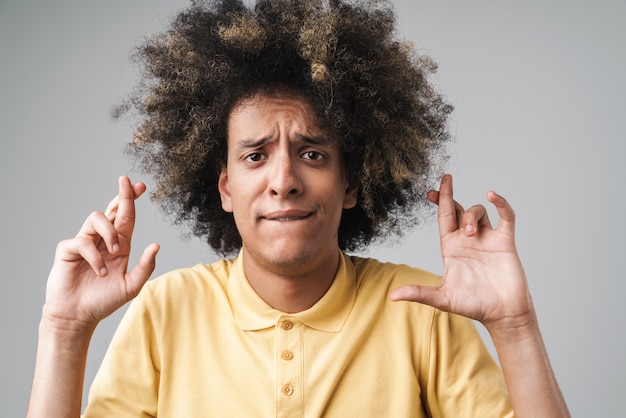 gespannen blanke man met afro-kapsel fronst en houdt de vingers gekruist geïsoleerd over grijze muur