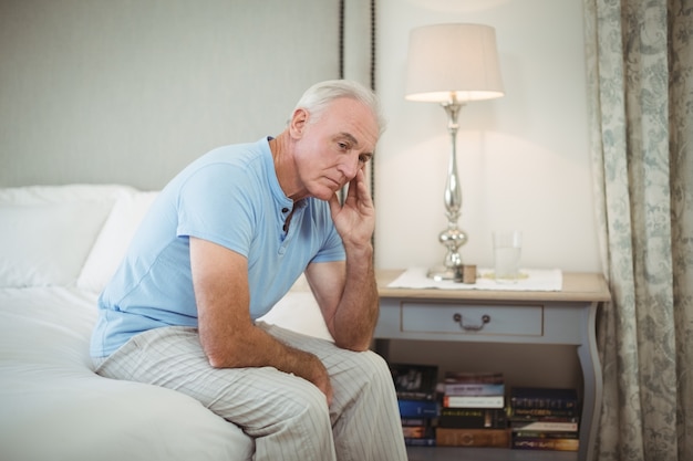 Gespannen hogere mensenzitting op bed in slaapkamer