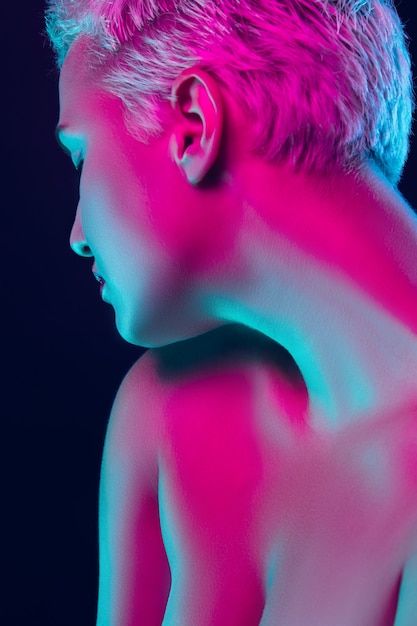 gespannen. Portret van vrouwelijke mannequin in neonlicht op donkere studioachtergrond. Mooie blanke vrouw met trendy make-up en verzorgde huid. Levendige stijl, schoonheidsconcept. Detailopname. Copyspace