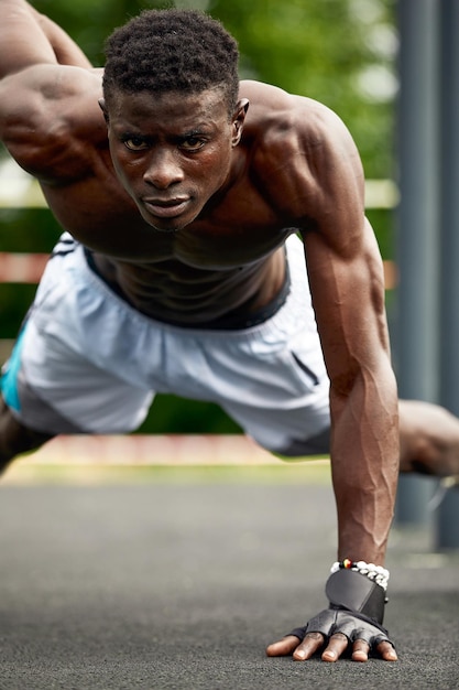 Gespierde Afrikaanse man doet push-ups tegen blauwe lucht Sterke mannelijke atleet die buitenshuis traint