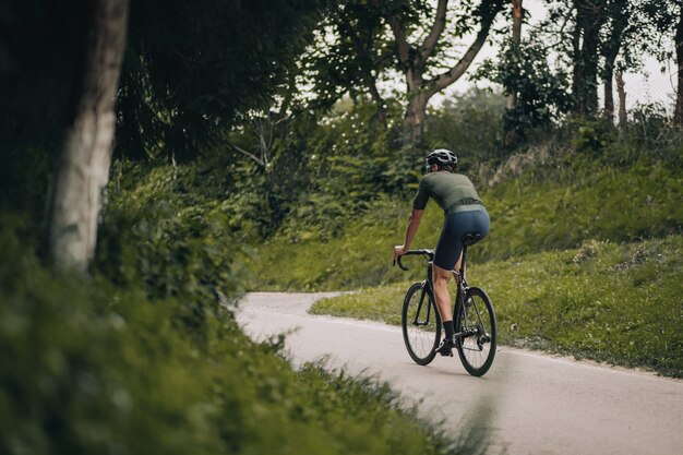 Gespierde blanke man in sportkleding en helm fietsen tijdens de ochtend buiten. Professionele sportman met actieve training in groen stadspark.