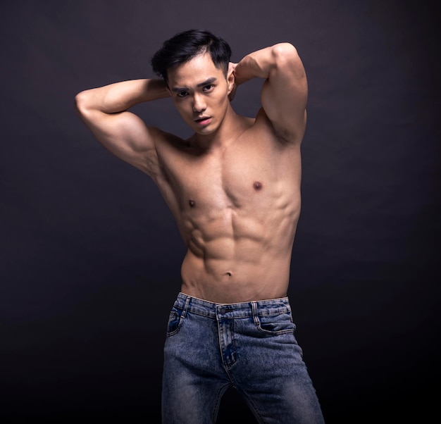Gespierde bodybuilder Aziatische man doet poseren op zwarte achtergrond