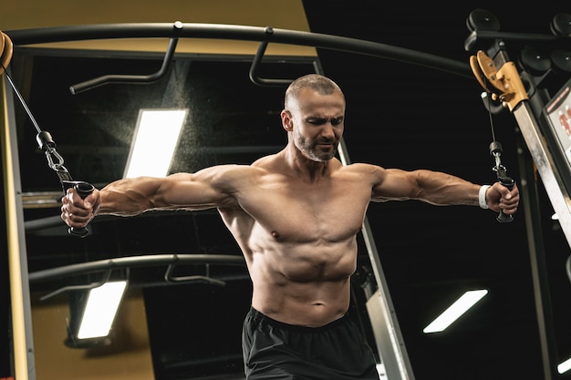 Gespierde bodybuilder doet kabel-crossover-oefening voor een borst tijdens zijn training in de sportschool