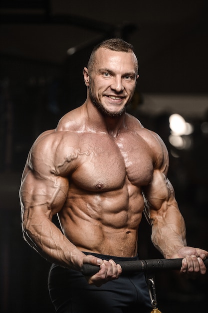 Gespierde bodybuilder fitness man doet armen oefeningen in de sportschool