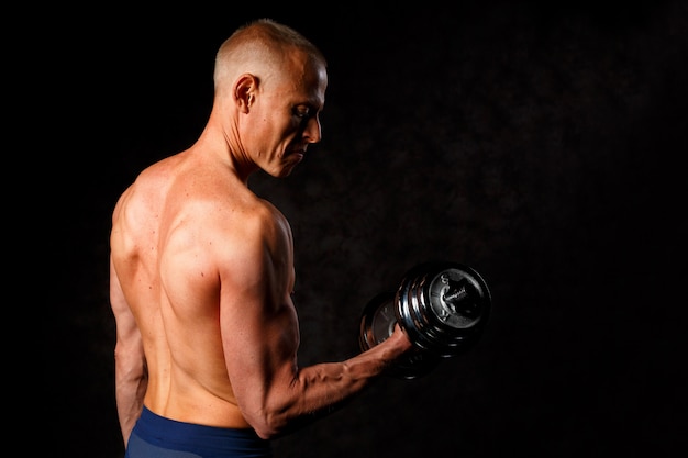 Gespierde bodybuilder man doen oefeningen met halter op zwarte achtergrond