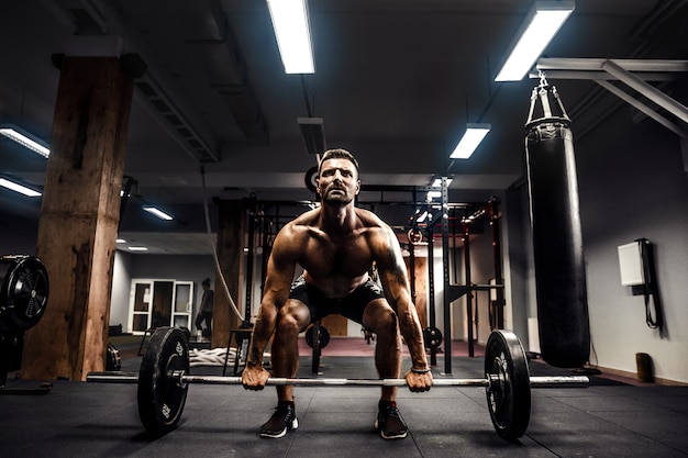 Gespierde fitness man doen deadlift een halter boven zijn hoofd in het moderne fitnesscentrum