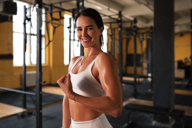 Gespierde fitte vrouw die in de sportschool staat en naar de camera kijkt.