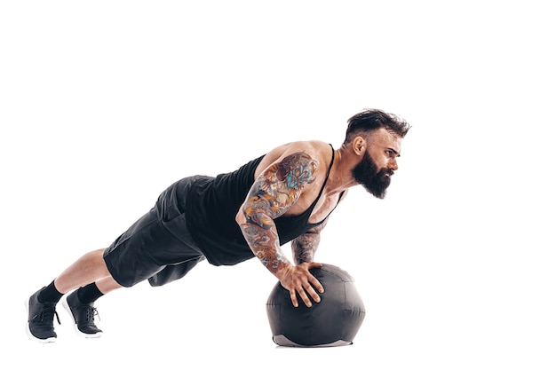 Gespierde getatoeëerde bebaarde man fitness gewichten uit te oefenen Medicine Ball push-ups oefeningen