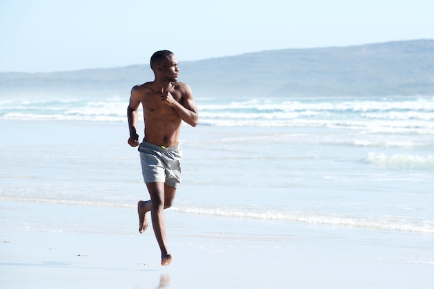 Gespierde jonge Afrikaanse man loopt langs het strand