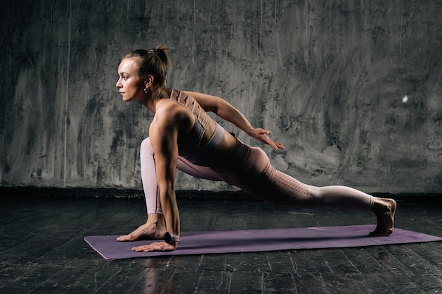 Gespierde jonge atletische vrouw met mooi lichaam die sportkleding draagt die houding op yogamat oefent