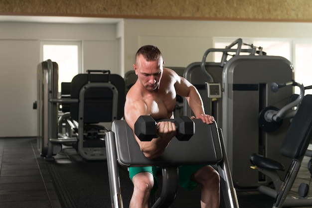 Gespierde jonge man doet zwaar gewicht oefening voor biceps met halters in moderne fitnesscentrum sportschool