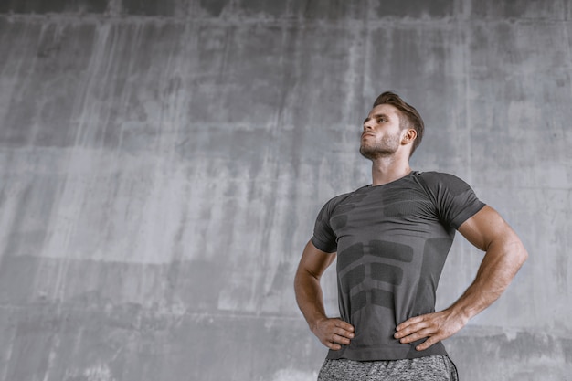 Gespierde jonge man in mode sportkleding op grijze muur.