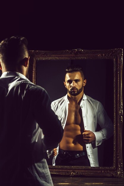 Foto gespierde macho man met sexy atleet lichaam in de buurt van vintage spiegel
