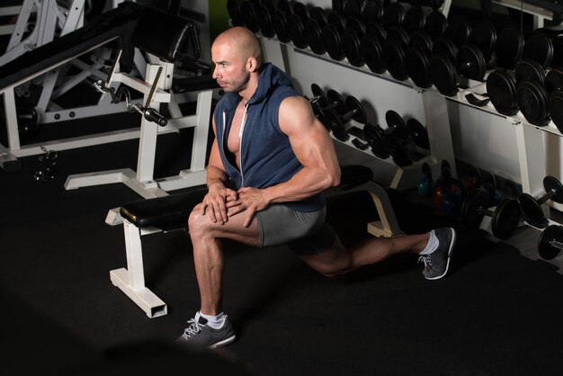 Gespierde man die zijn been op de vloer in een sportschool strekt en spieren buigt Gespierde atletische bodybuilder Fitness Model