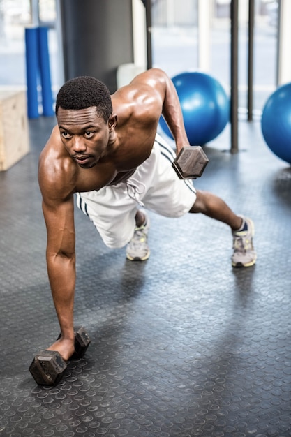 Gespierde man doen push-up met halters in de sportschool CrossFit