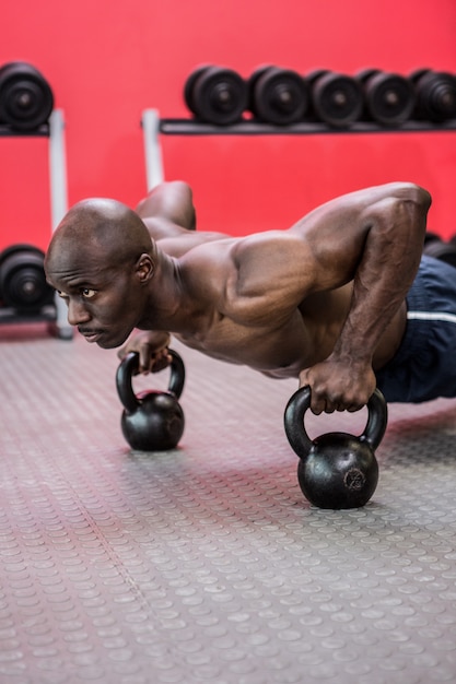 Gespierde man doet push-ups met kettlebells