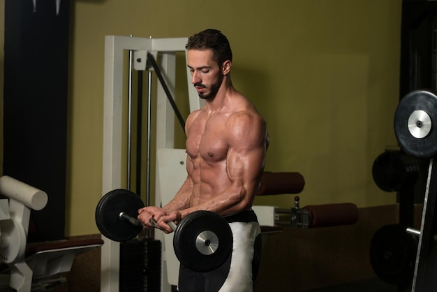 Gespierde man doet zware oefening voor biceps met barbell in sportschool