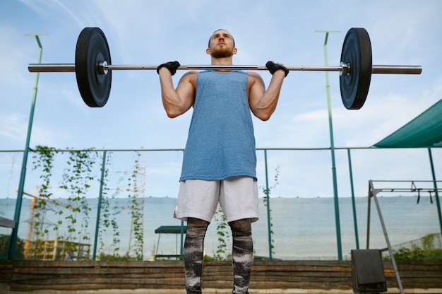 Gespierde man houdt barbell op zijn borst, straattraining