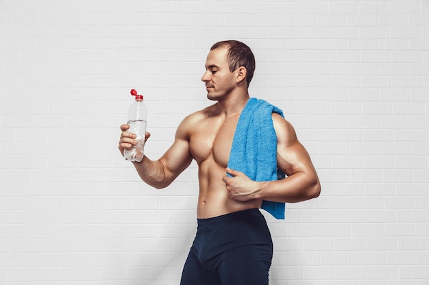 Gespierde man houdt een fles water vast terwijl hij sportkleding draagt met een handdoek geïsoleerd op een witte achtergrond