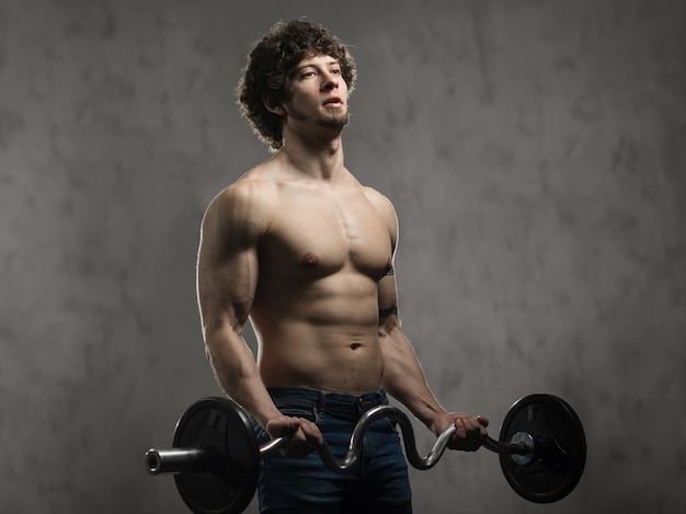 Gespierde man traint biceps met barbell in de sportschool, hand opleiding