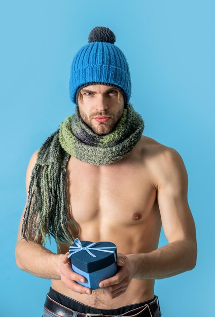 gespierde man Valentijnsdag aanwezig geïsoleerd op blauw man in gebreide kleding houd cadeau voor Valentijnsdag in studio gespierde man op Valentijnsdag met huidige foto van sexy gespierde man Valentijnsdag aanwezig