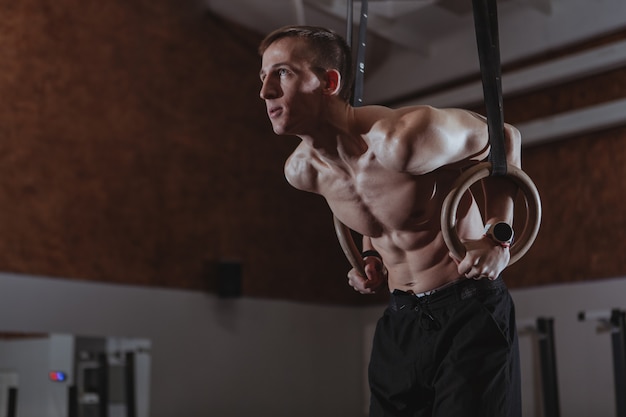 Gespierde mannelijke crossfit atleet trainen op gymnastiek ringen